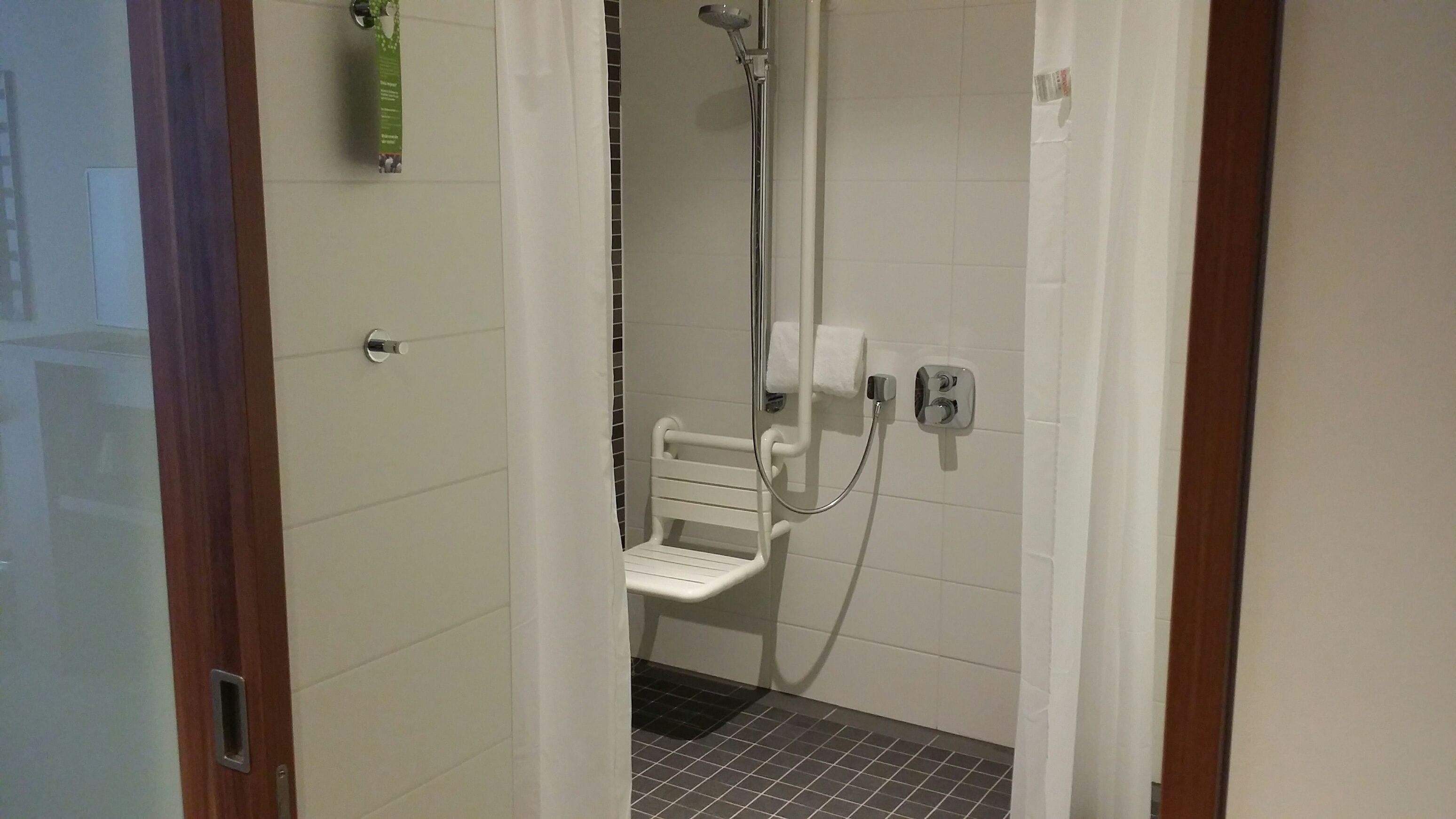 A small, tiled bathroom with a shower, a white toilet, and a grab bar.