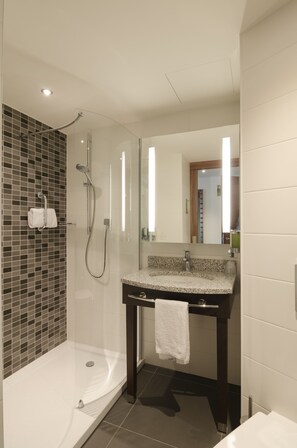 A modern bathroom with a glass-enclosed shower, a freestanding bathtub, and a vanity with a mirror. - Hampton by Hilton Frankfurt City Centre (Frankfurt)