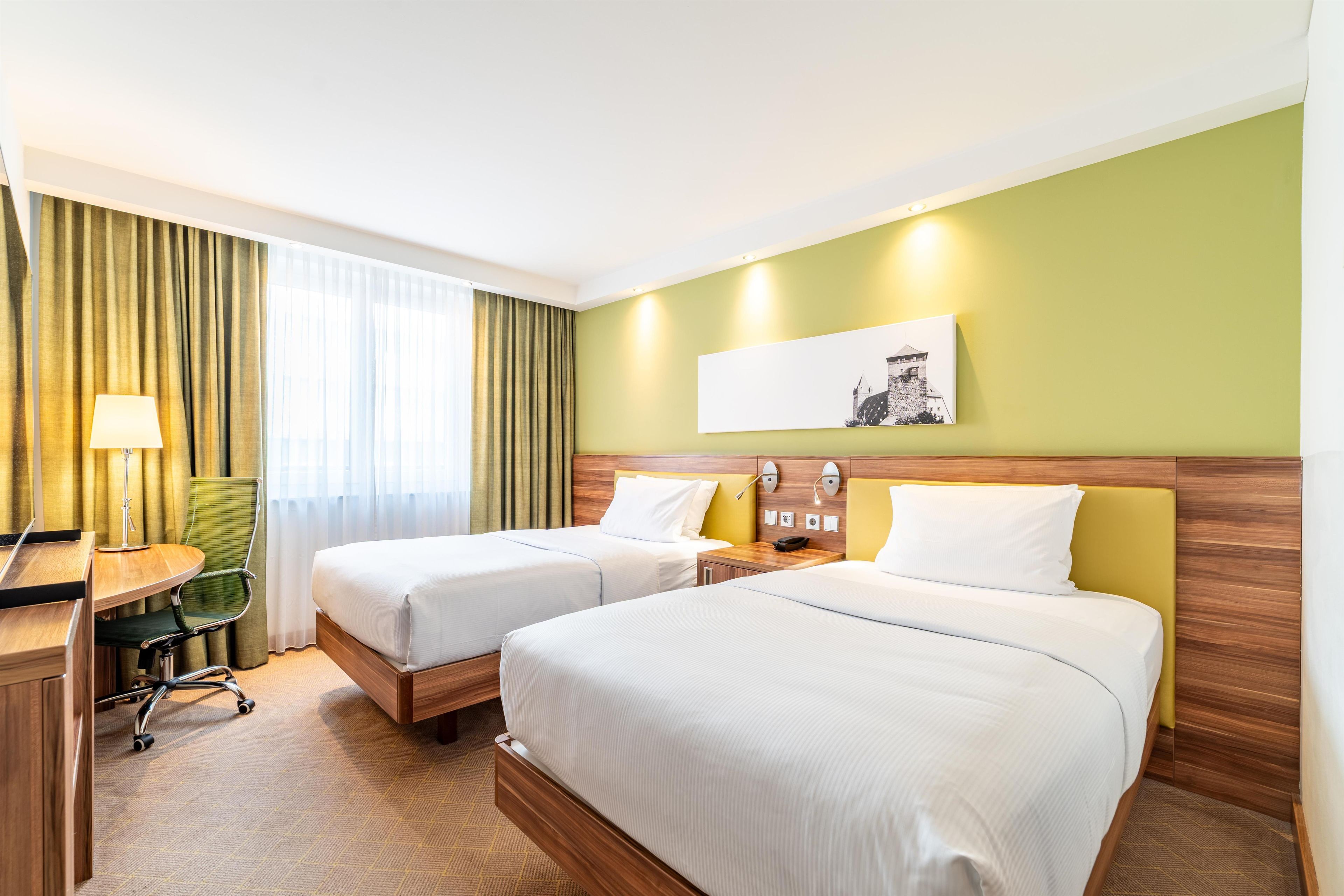 Une chambre d’hôtel avec deux lits, un bureau, une chaise, une lampe et un tableau au mur.