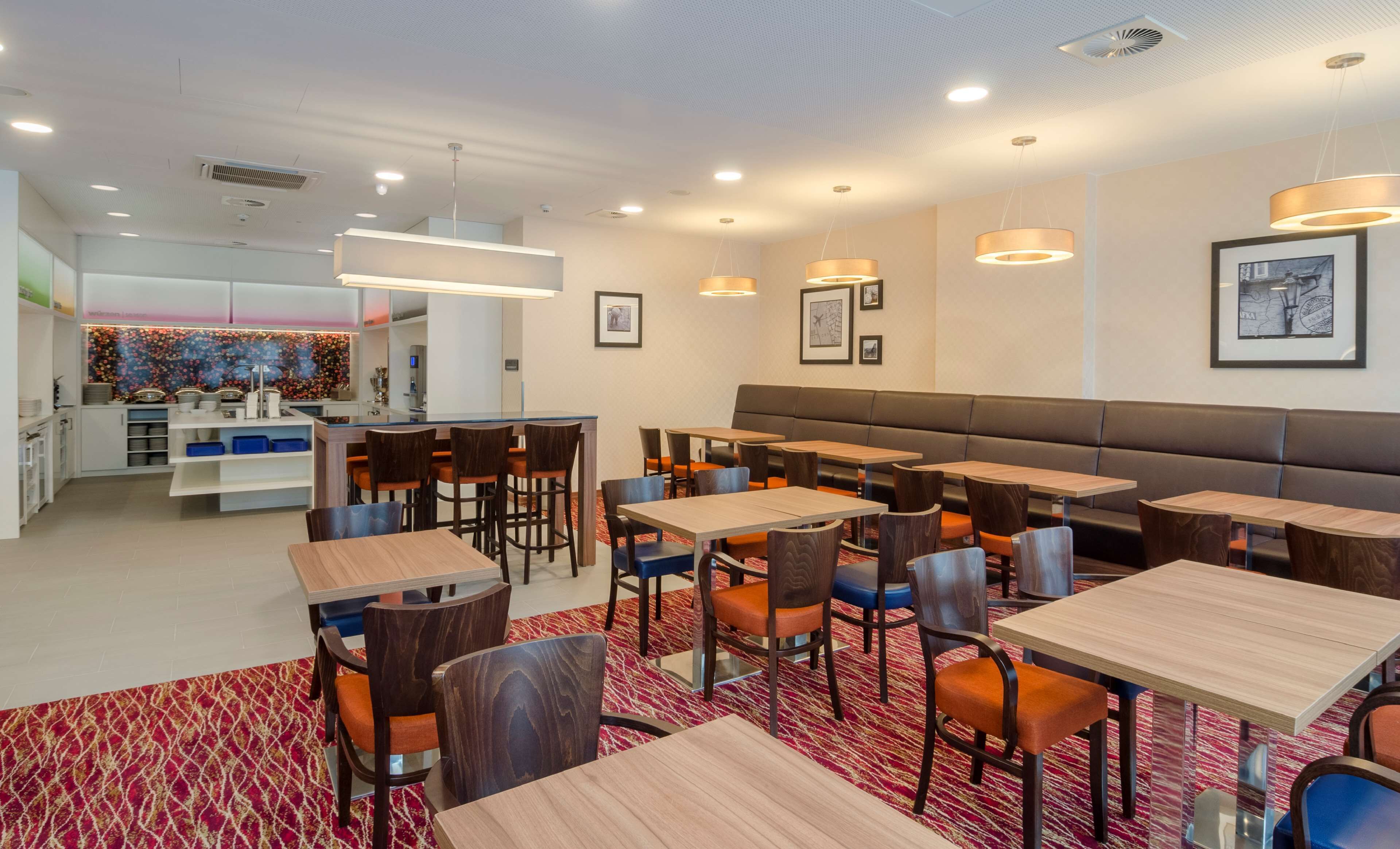 A modern restaurant with multiple tables and booths, a bar area, and a kitchen in the background.