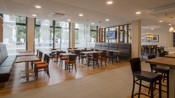 A modern restaurant with large windows, wooden tables, and comfortable seating areas. - Hampton by Hilton Frankfurt City Centre (Frankfurt)