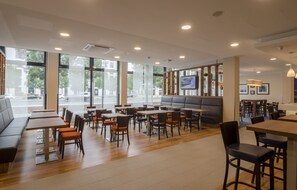 A modern restaurant with large windows, wooden tables, and comfortable seating areas. - Hampton by Hilton Frankfurt City Centre (Frankfurt)