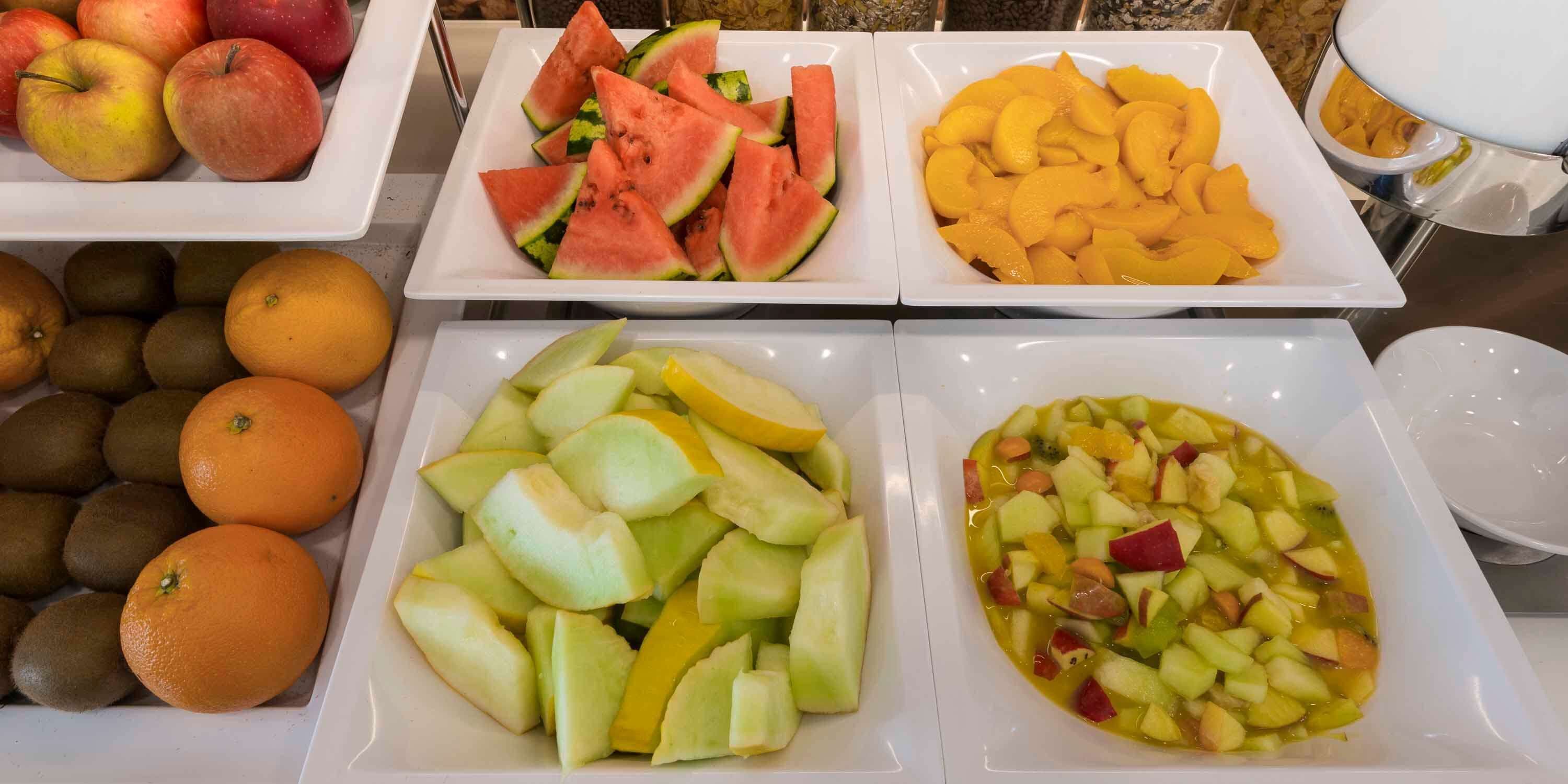 A buffet with various fruits including apples, watermelon, peaches, oranges, and kiwi.