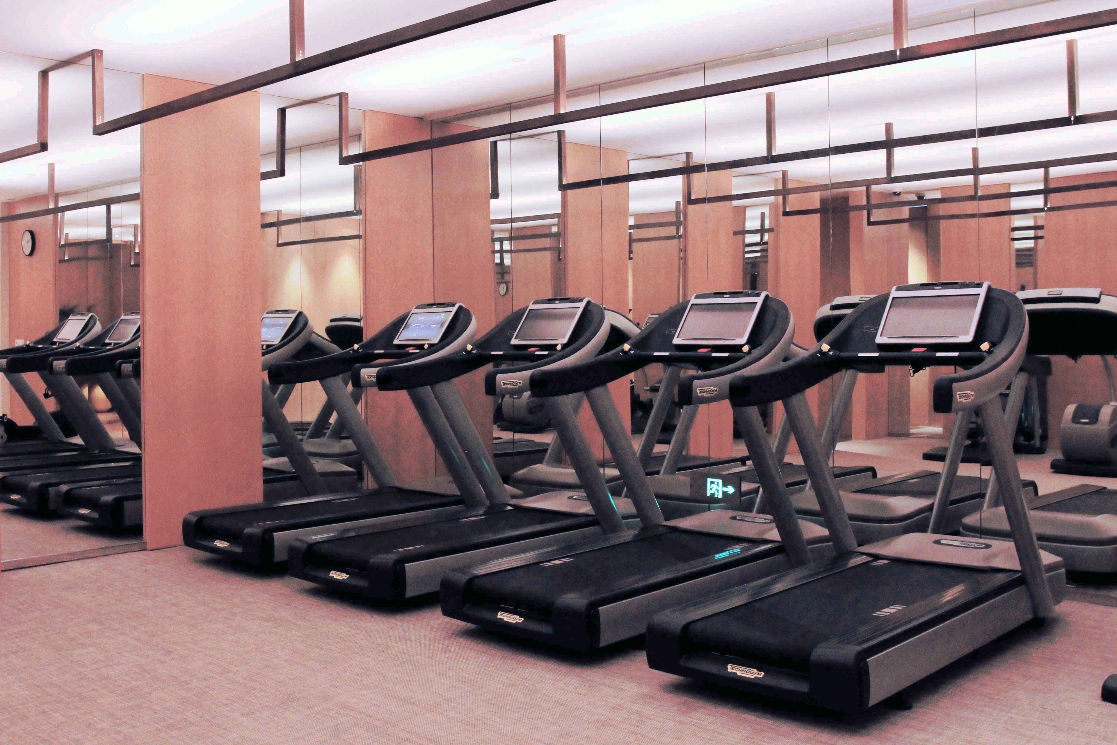 A row of treadmills in a gym with mirrored walls and wooden paneling.