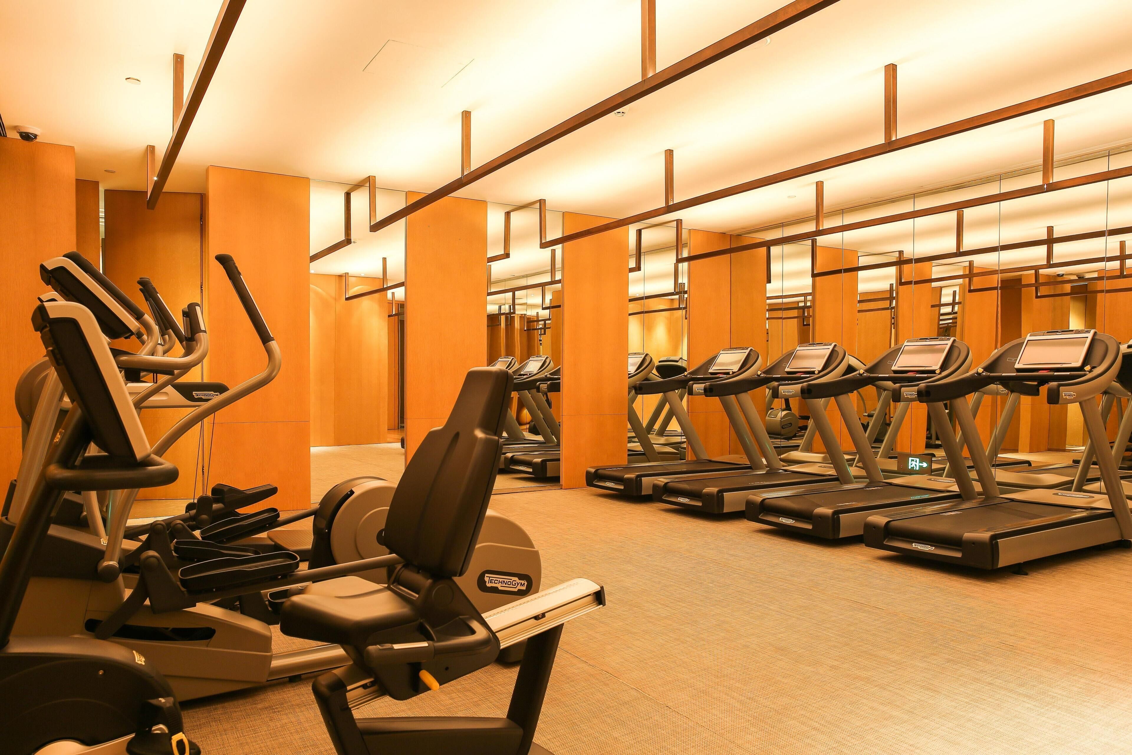 Un gimnasio con varias cintas de correr y elípticas, paredes de madera y suelo alfombrado.