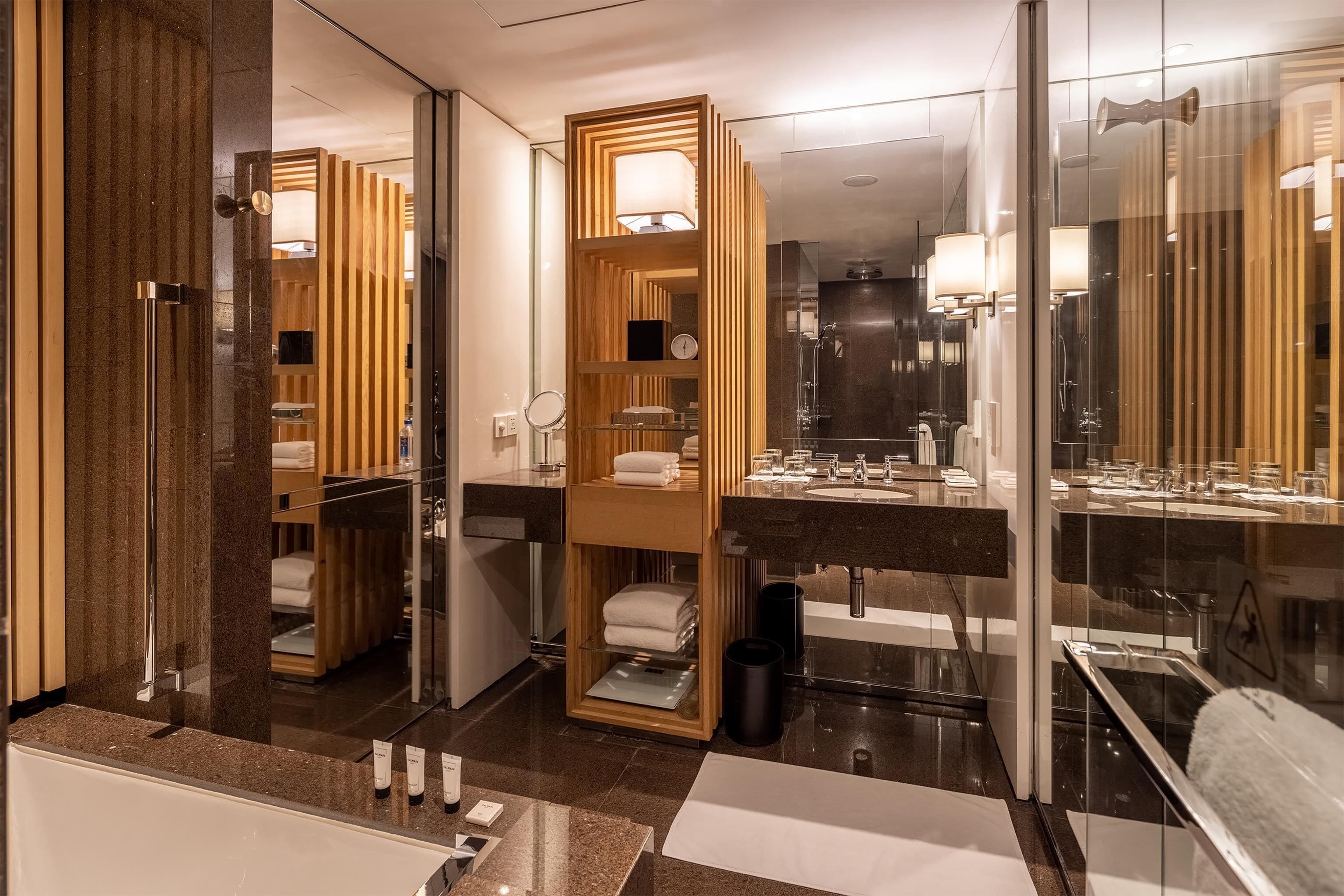 Une salle de bain moderne avec un grand miroir, un meuble-lavabo en bois, une cabine de douche en verre et un plan de toilette en marbre.