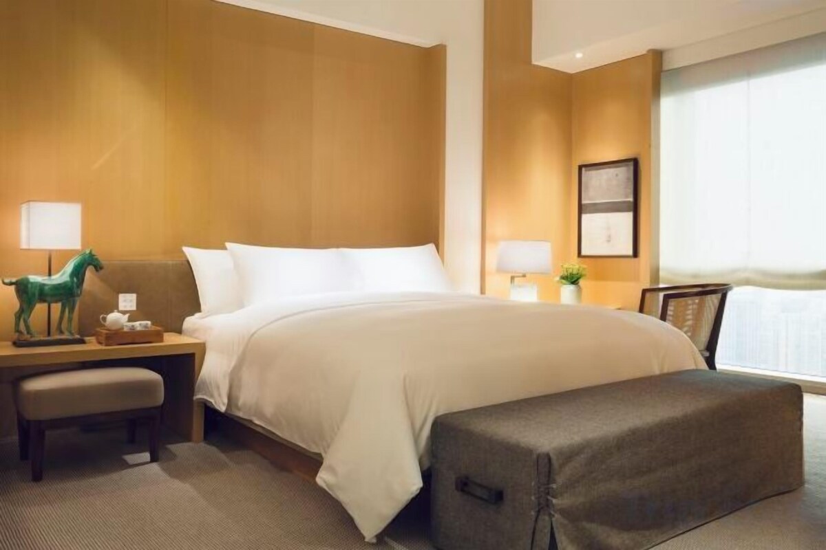Ein Hotelzimmer mit einem großen Bett, Nachttischen, einem Schreibtisch und einem Fenster mit Jalousien.