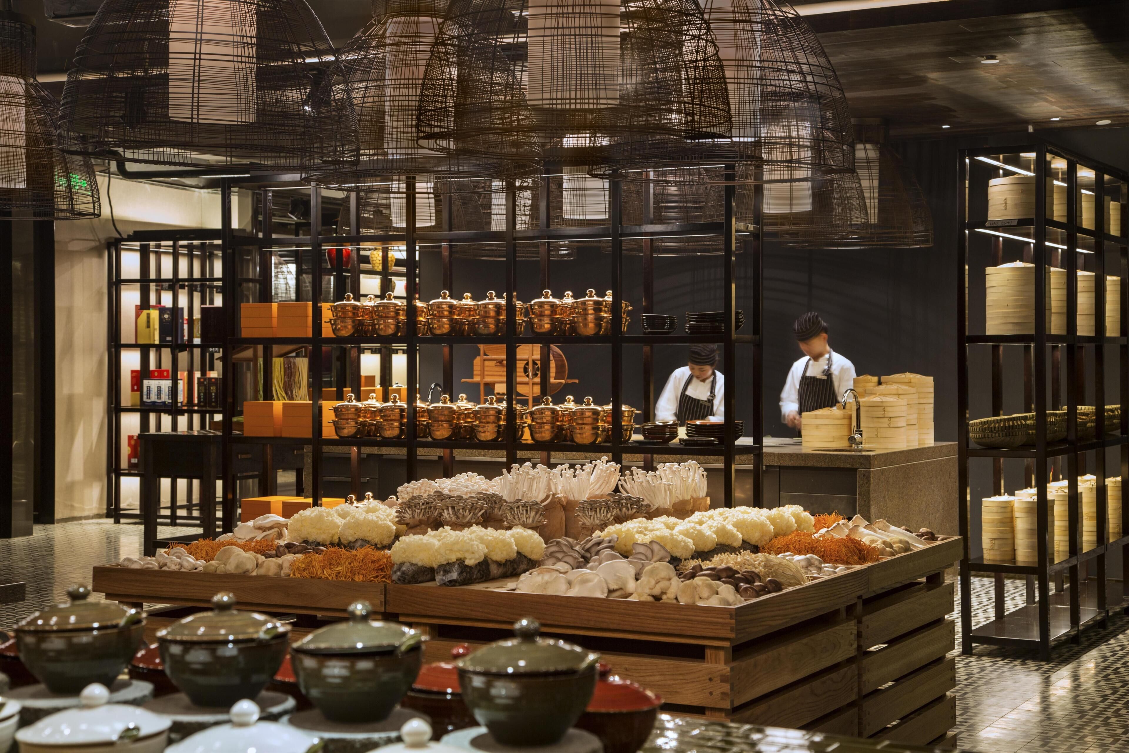 A restaurant interior with a chef at the counter, wooden crates with food items, and shelves with kitchenware.