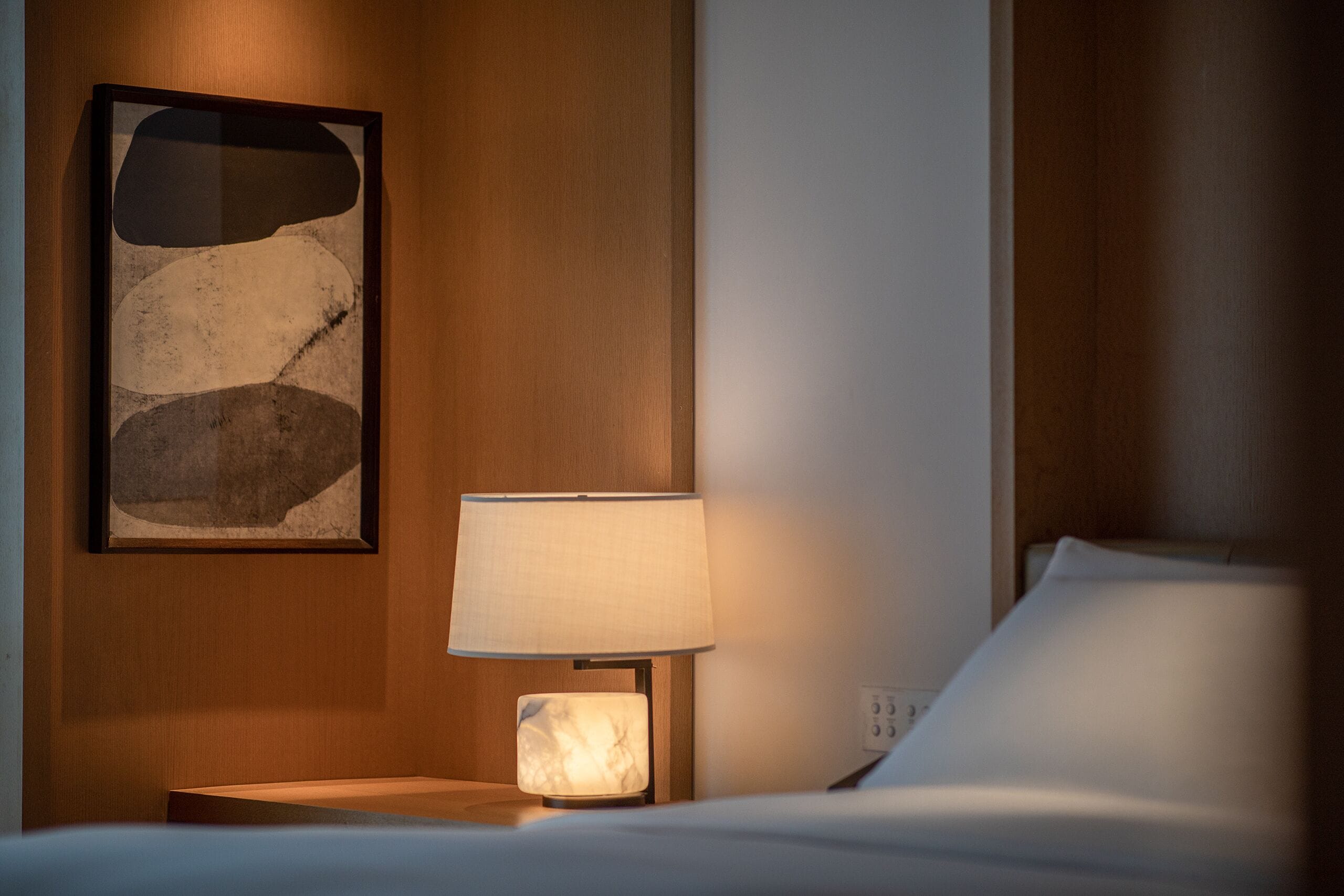 Une chambre d’hôtel avec un lit, une table de chevet dotée d’une lampe et une œuvre d’art abstraite encadrée accrochée au mur.