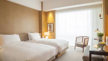 A hotel room with two beds, a desk, a chair, and a large window with curtains.