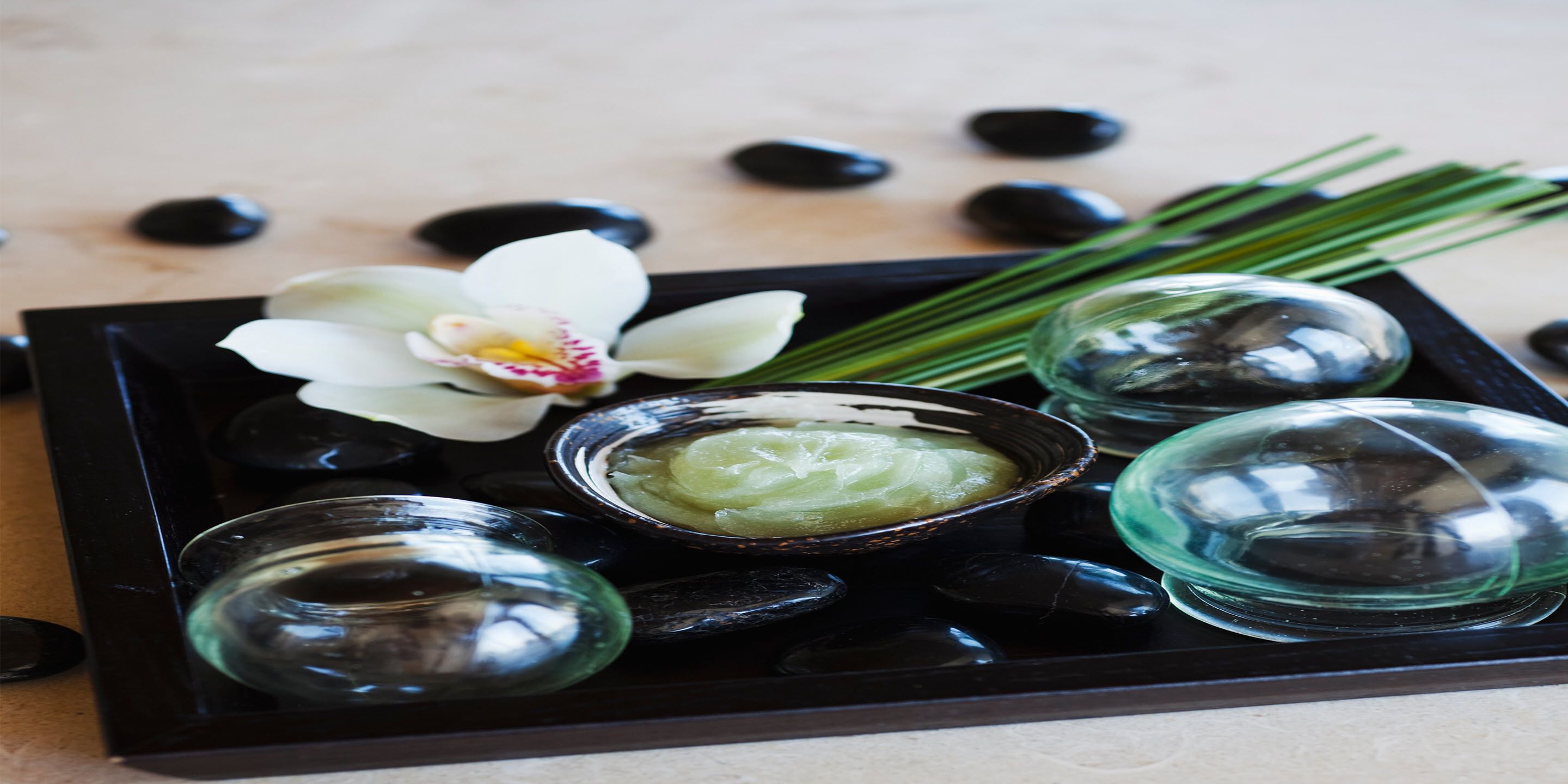 Un plateau contenant des pierres noires, une orchidée blanche et un bol rempli d’une substance verte.