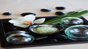 Un plateau contenant des pierres noires, une orchidée blanche et un bol rempli d’une substance verte.