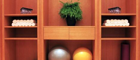 A wooden cabinet with shelves containing neatly rolled towels, a potted plant, and exercise balls.
