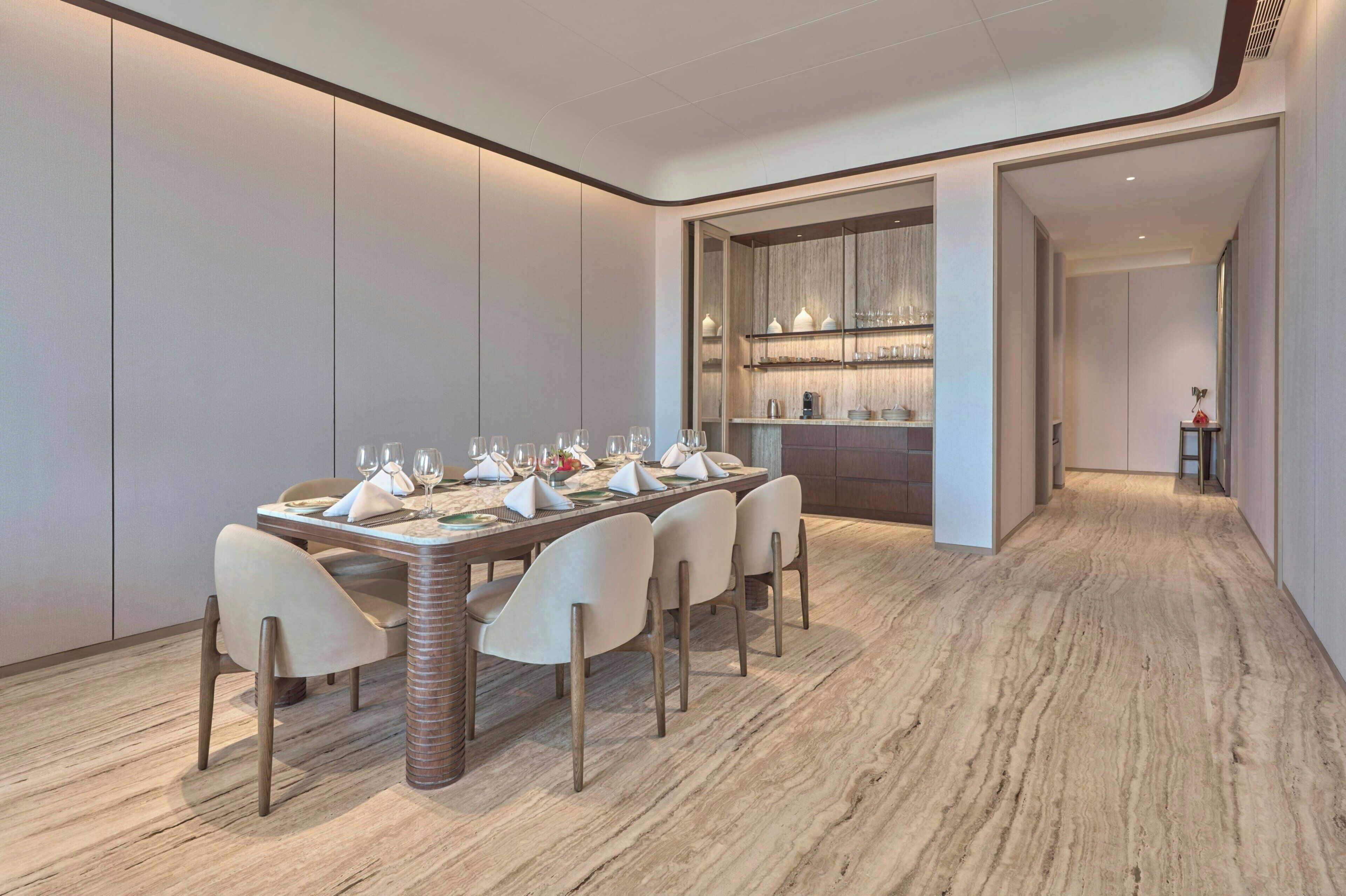 A modern dining area with a long table set for six, flanked by tall chairs, and a kitchen area with shelves above the counter.