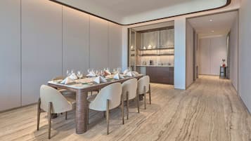 Un espace repas moderne avec une longue table dressée pour six personnes, entourée de chaises hautes, et un coin cuisine avec des étagères au-dessus du comptoir.