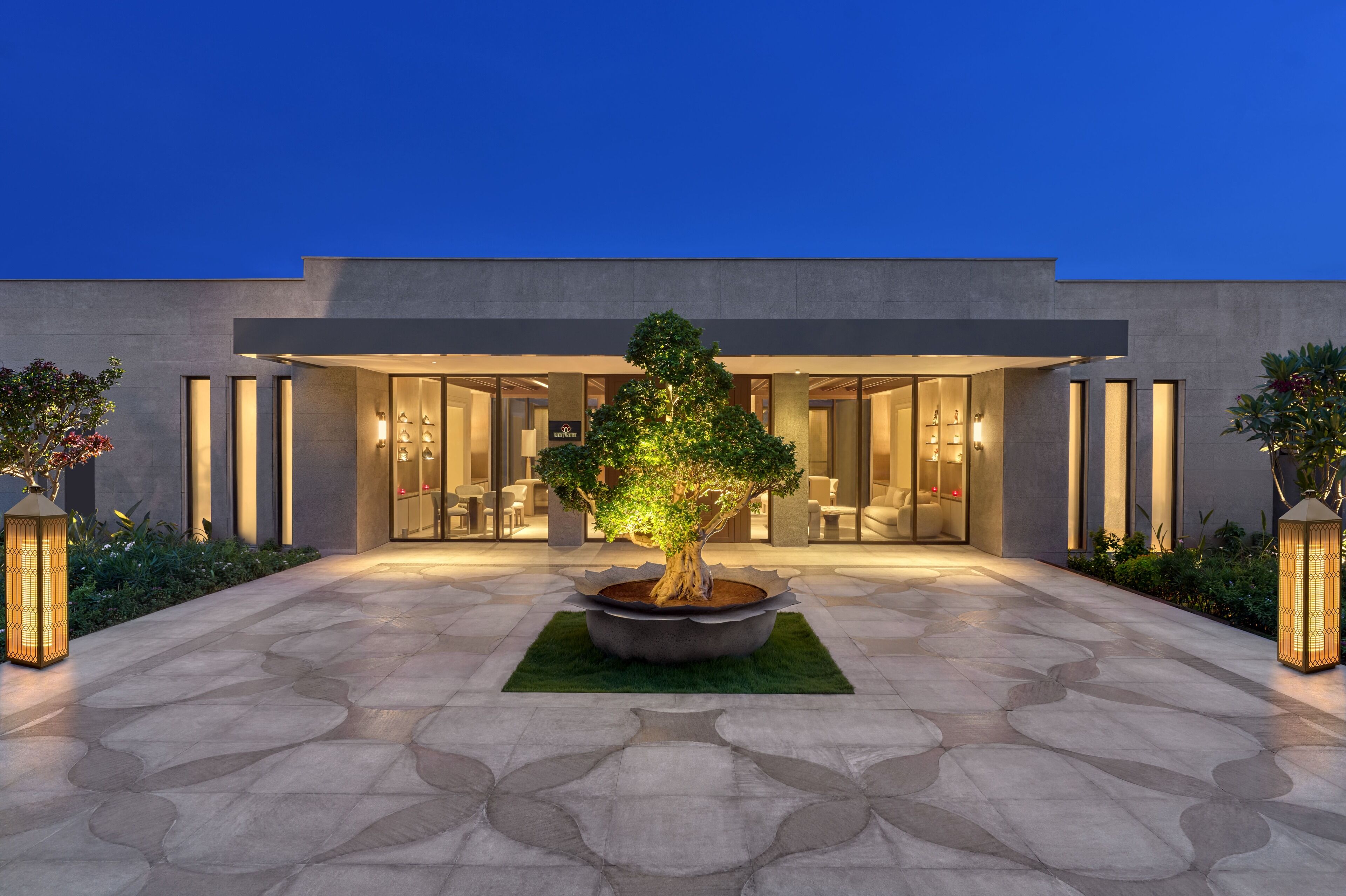 A modern building with a large entrance, a central tree, and a paved courtyard.