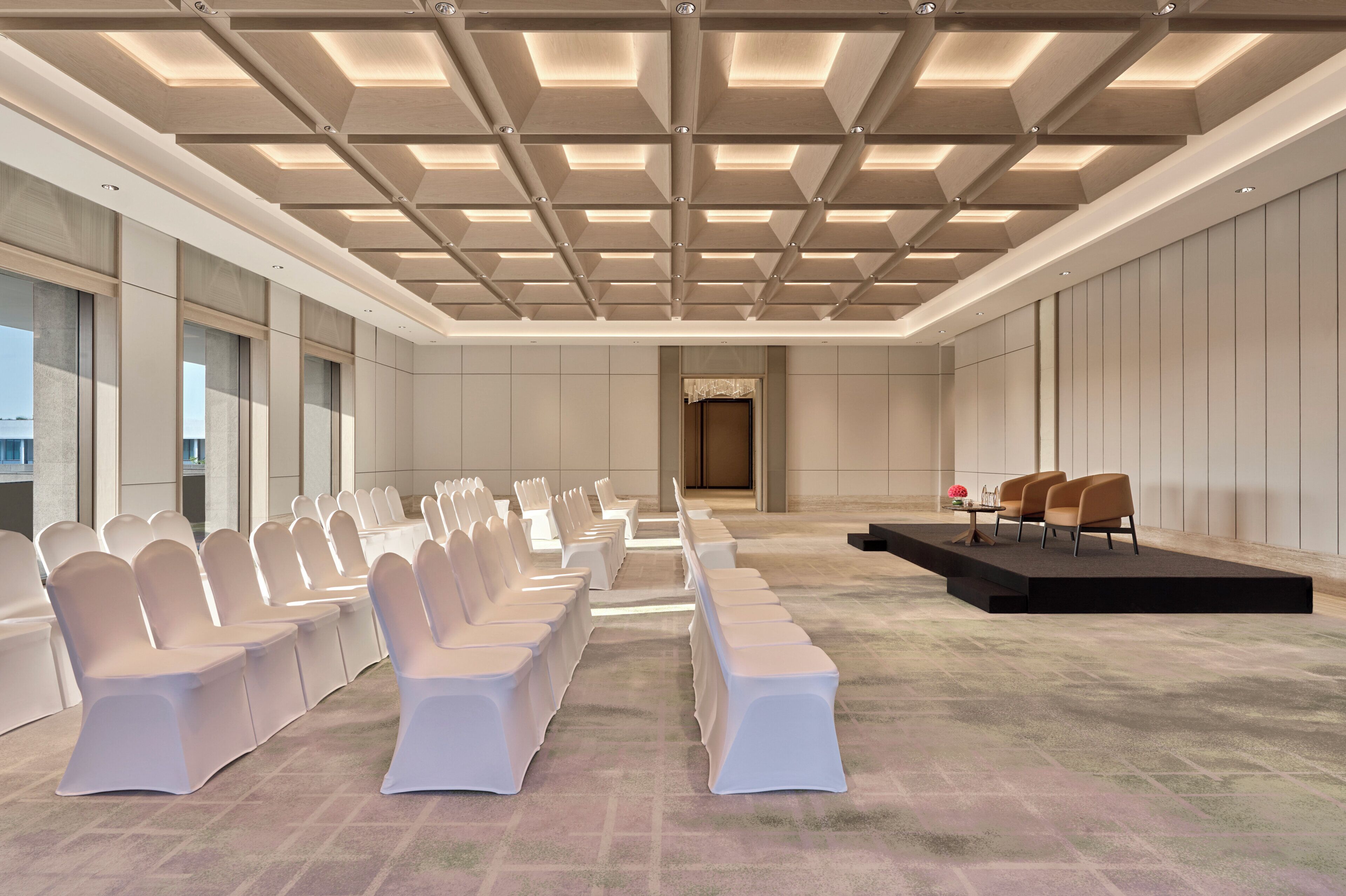 A conference room with rows of chairs, a stage, and a large window.
