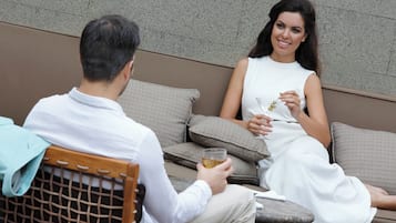 Un homme et une femme sont assis sur un canapé à motifs et discutent, chacun tenant un verre à la main.