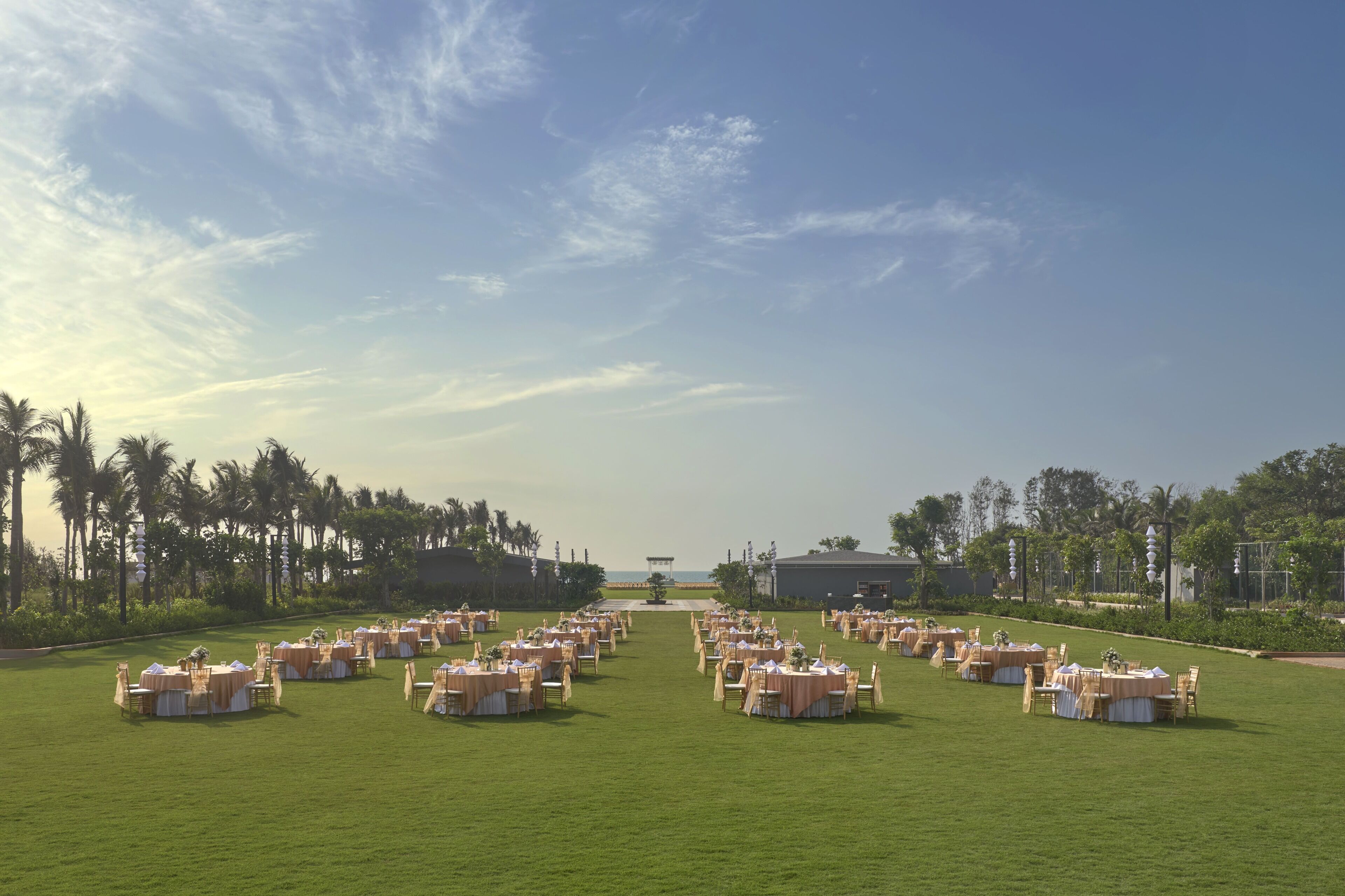 Salón de bodas al aire libre con varias mesas redondas y sillas, dispuestas en filas frente a un escenario.