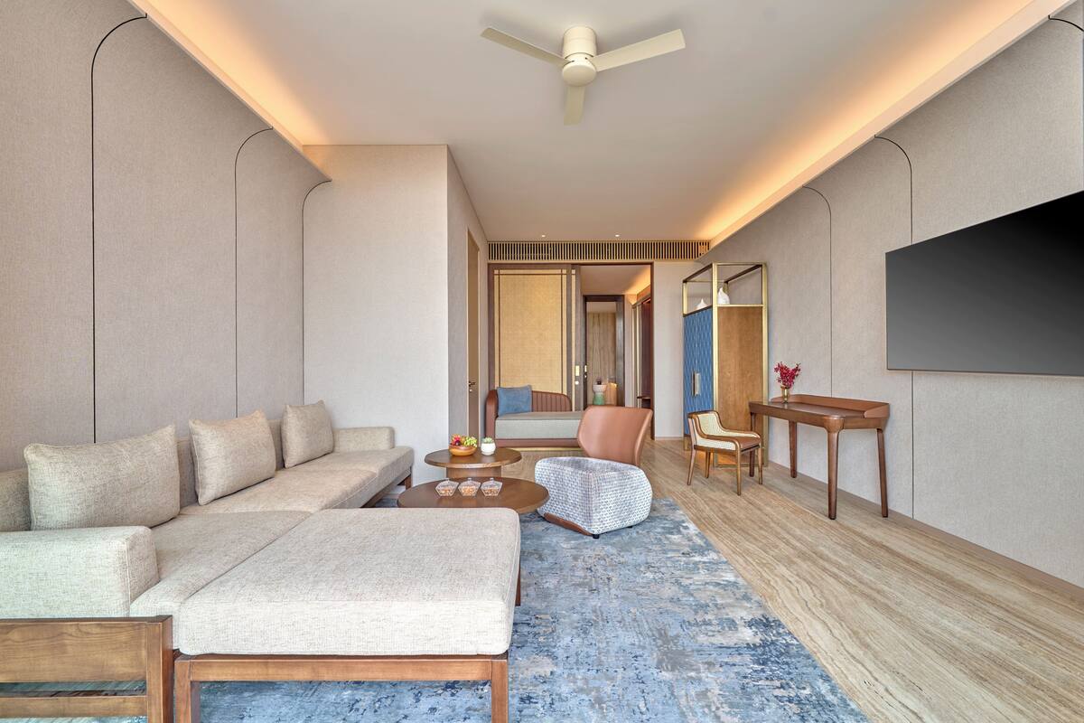 Ein modernes Hotelzimmer mit Sofa, Sesseln, Couchtisch und einem an der Wand befestigten Flachbildfernseher.