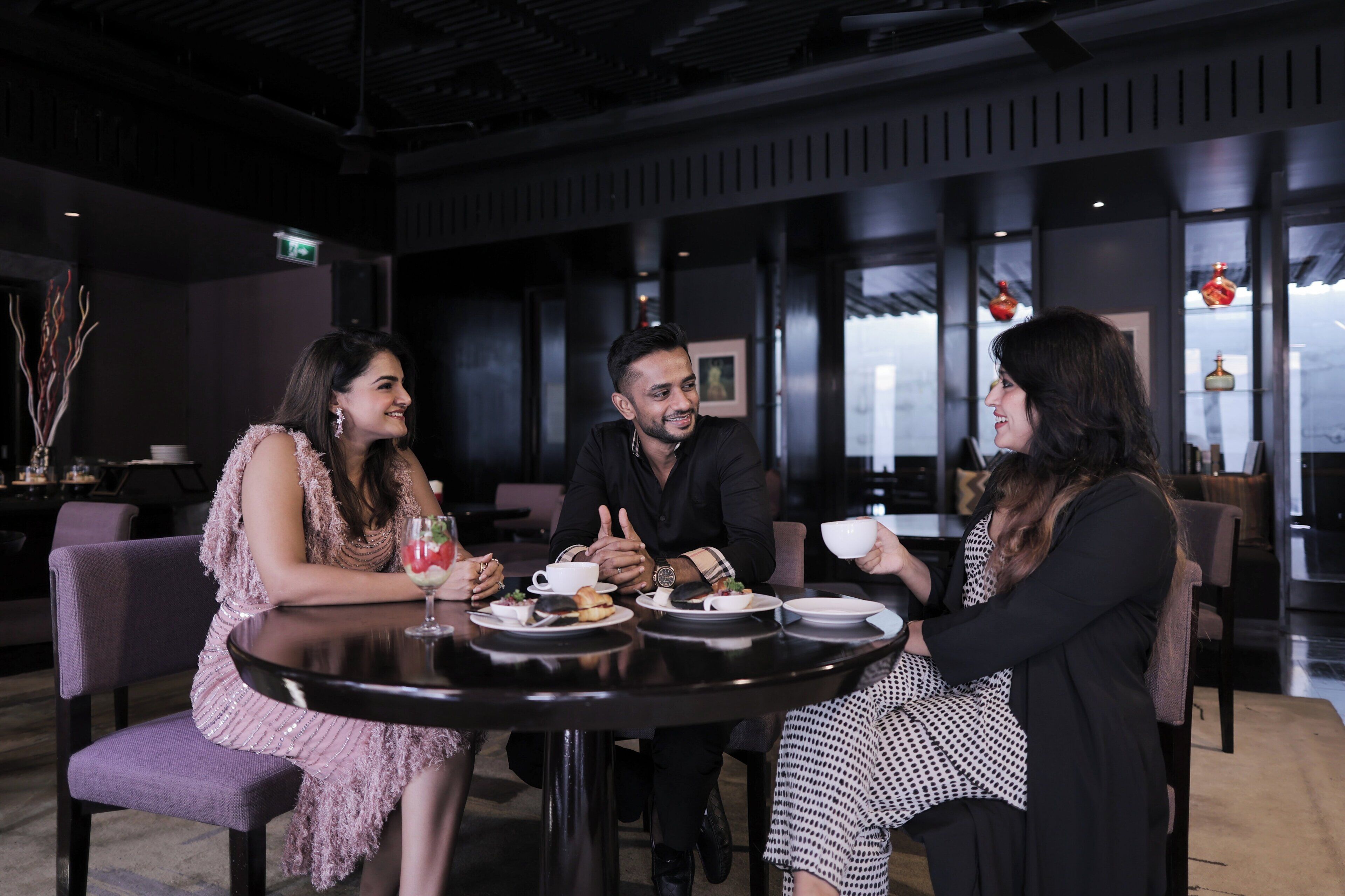 A group of people seated at a round table in a modern interior with dark tones and minimalistic decor.