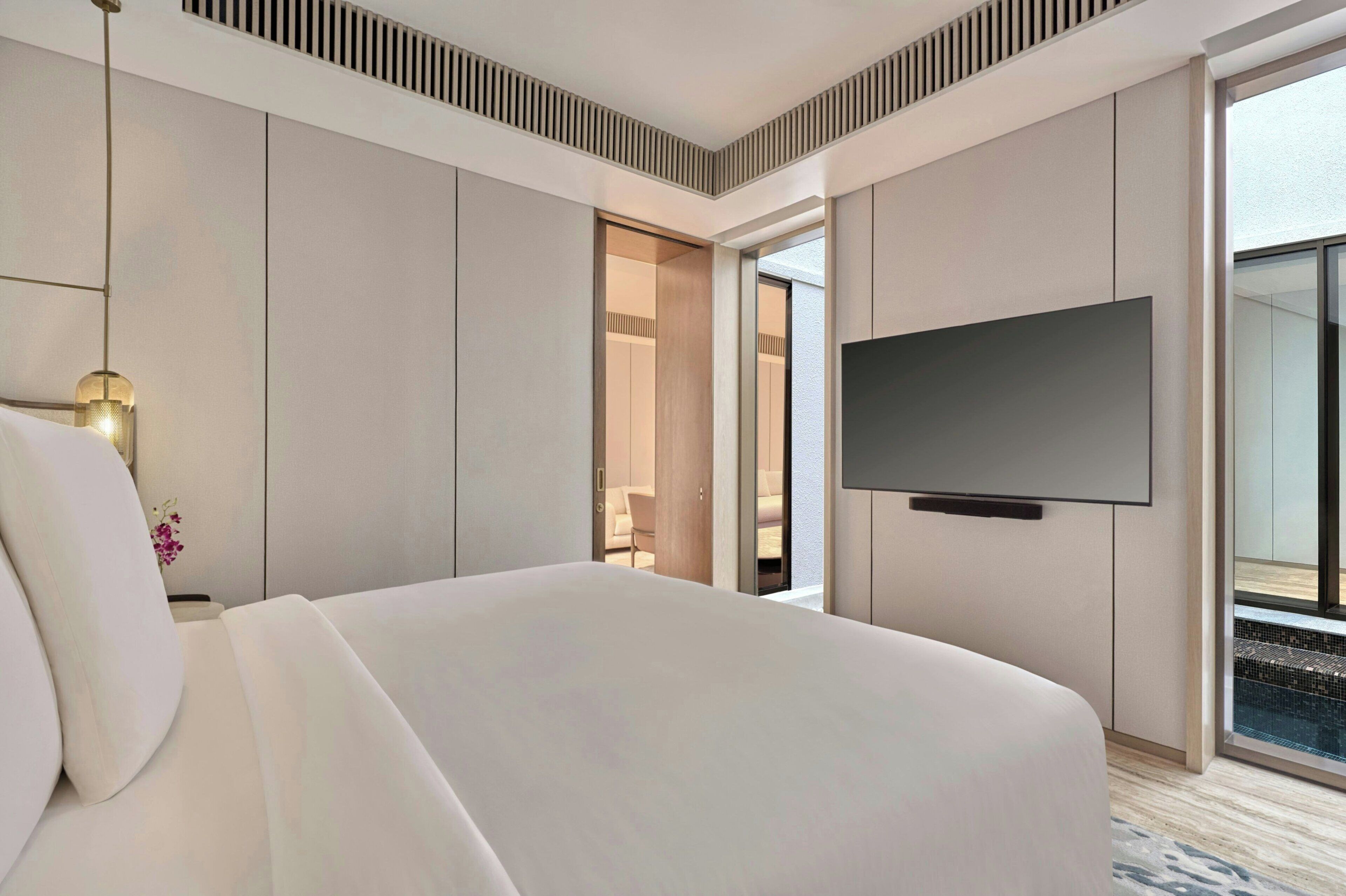 A hotel room with a large bed, a flat-screen TV mounted on the wall, and a view of the outdoors through a sliding door.