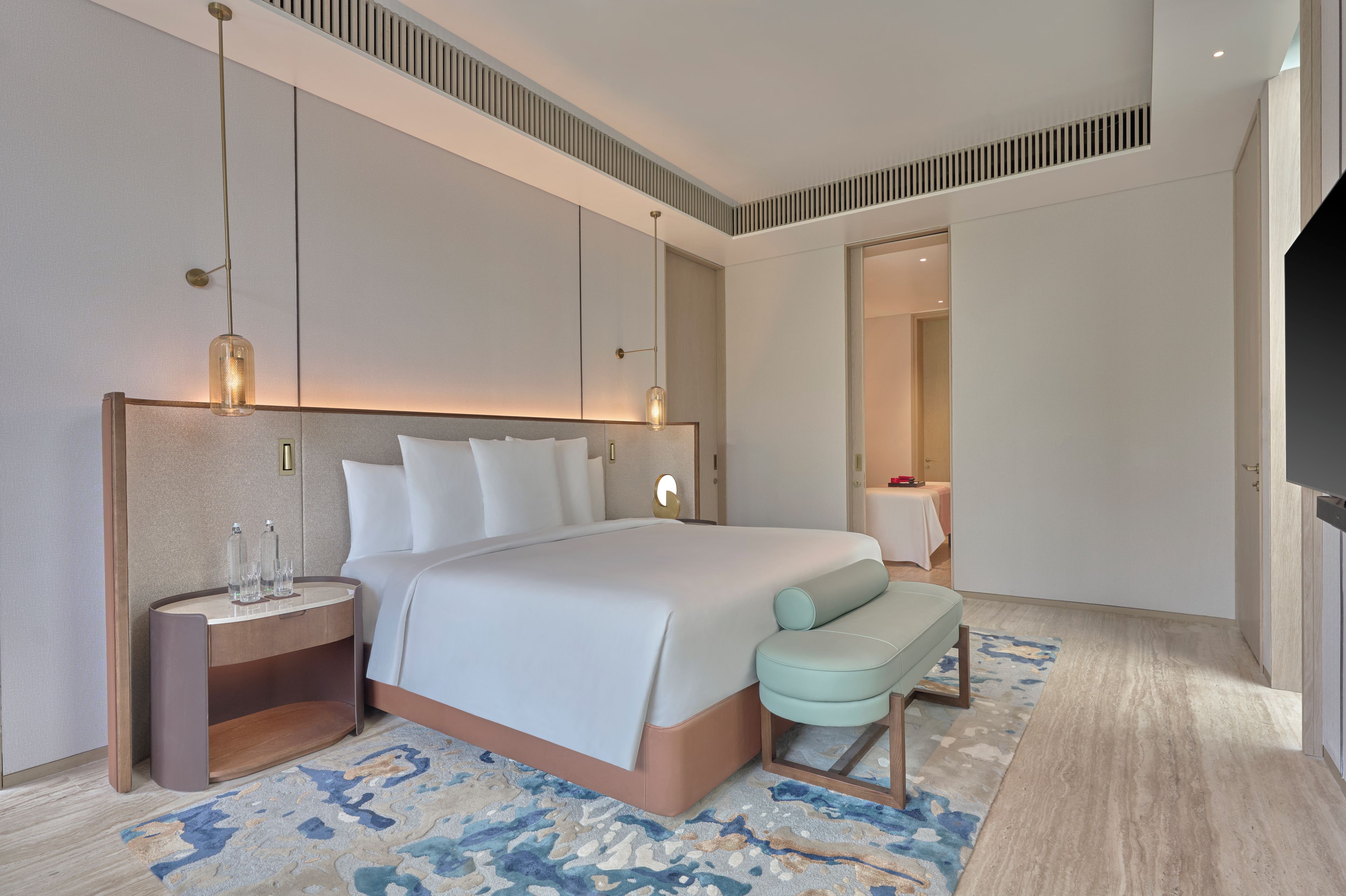 A modern hotel room with a large bed, bedside tables, a TV, and a bathroom visible through an open door.