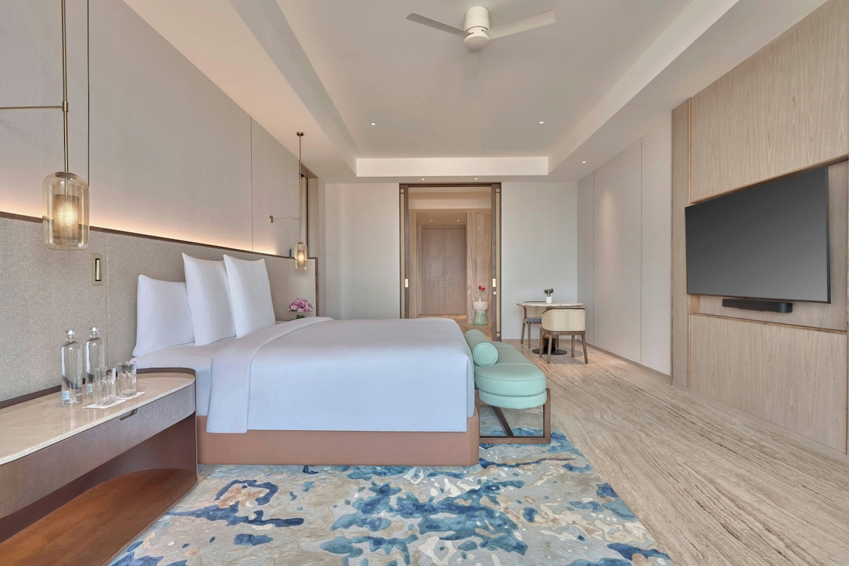 A hotel room with a bed, bedside table, TV, and a seating area with a chair and table.