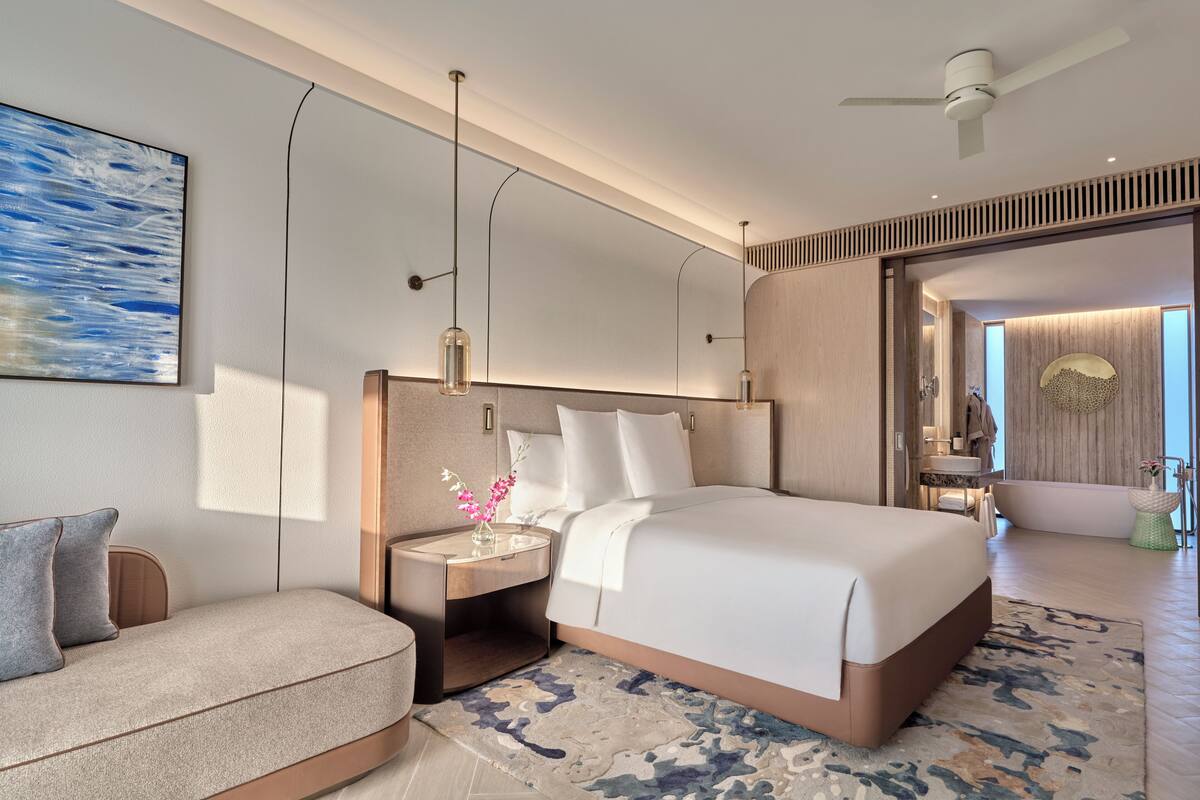 Ein modernes Hotelzimmer mit einem großen Bett, einer Sitzecke, einem Schminktisch und einem Deckenventilator.