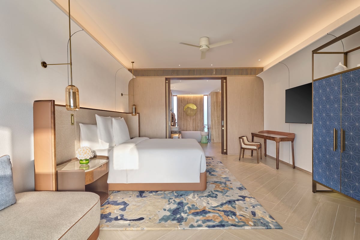 Ein modernes Hotelzimmer mit Bett, Nachttisch, Lampe und Fernseher.