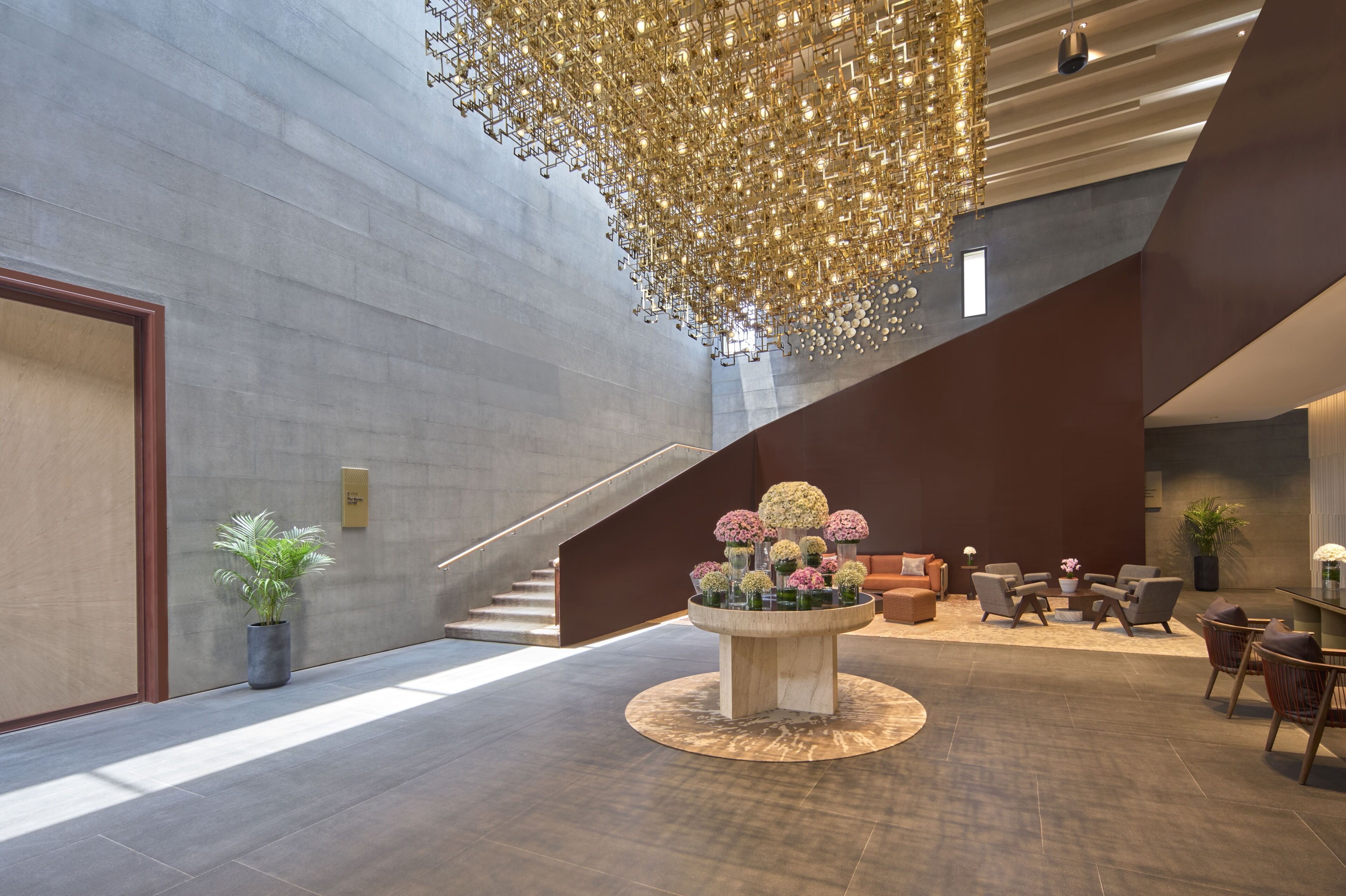 A modern lobby with a central floral arrangement, a staircase, and seating area.