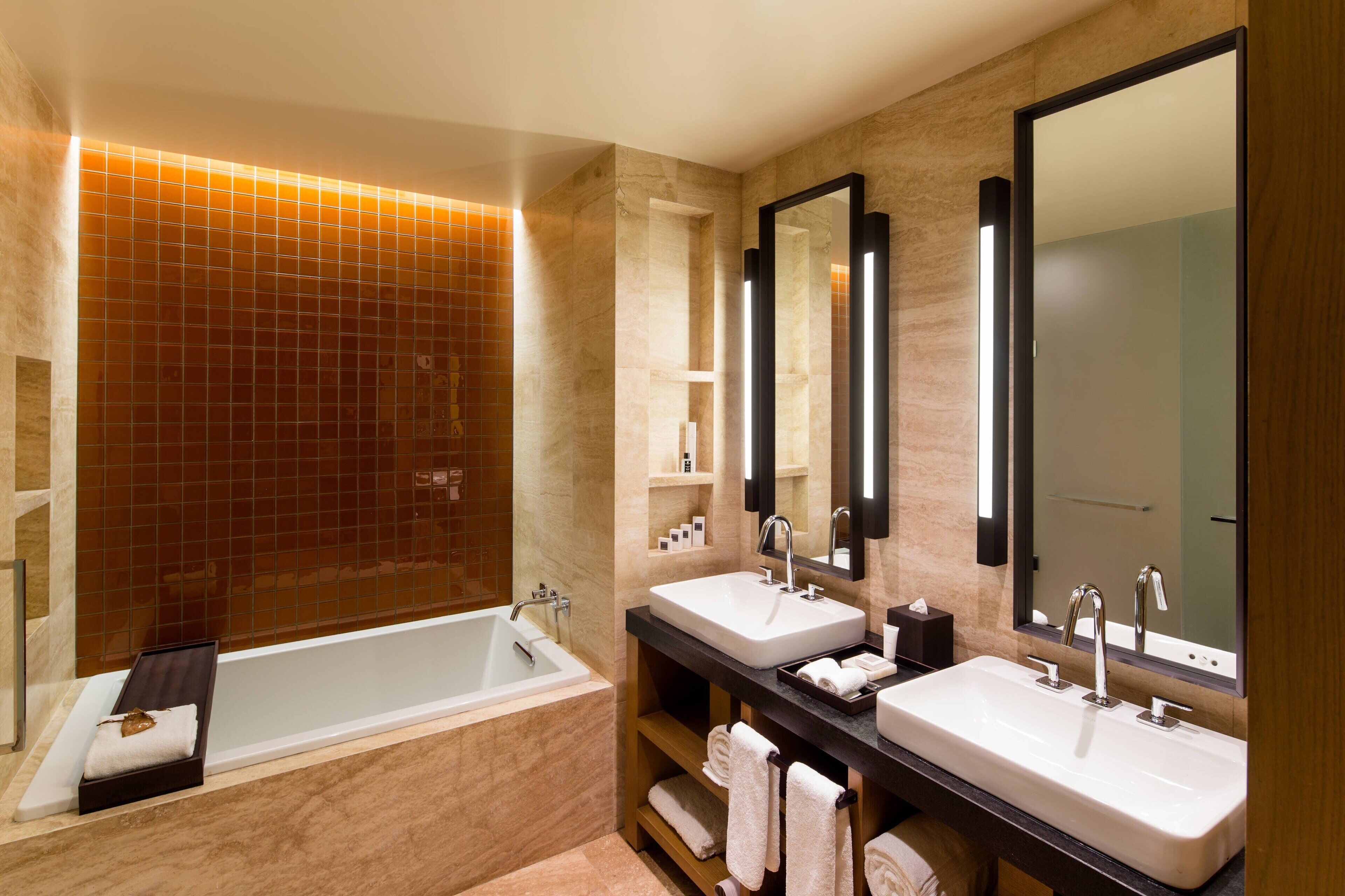 Un baño moderno con una bañera, dos lavamanos y espejos grandes.