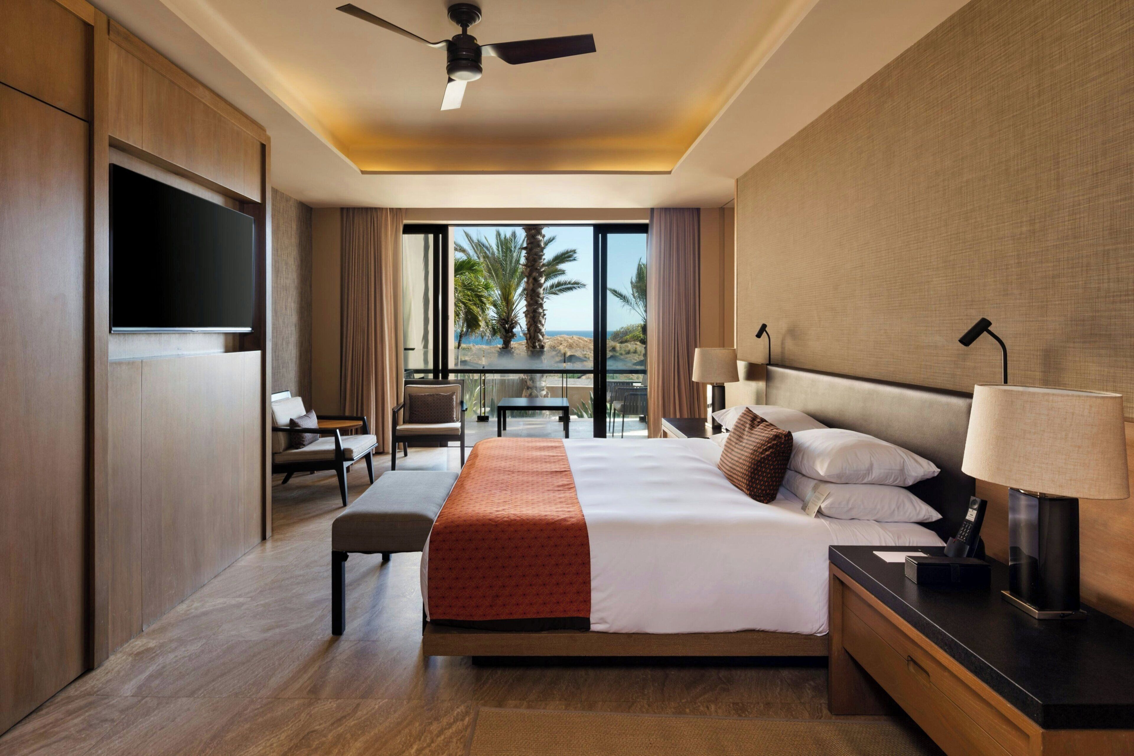 A hotel room with a bed, bedside table, lamp, TV, and a balcony with a view.