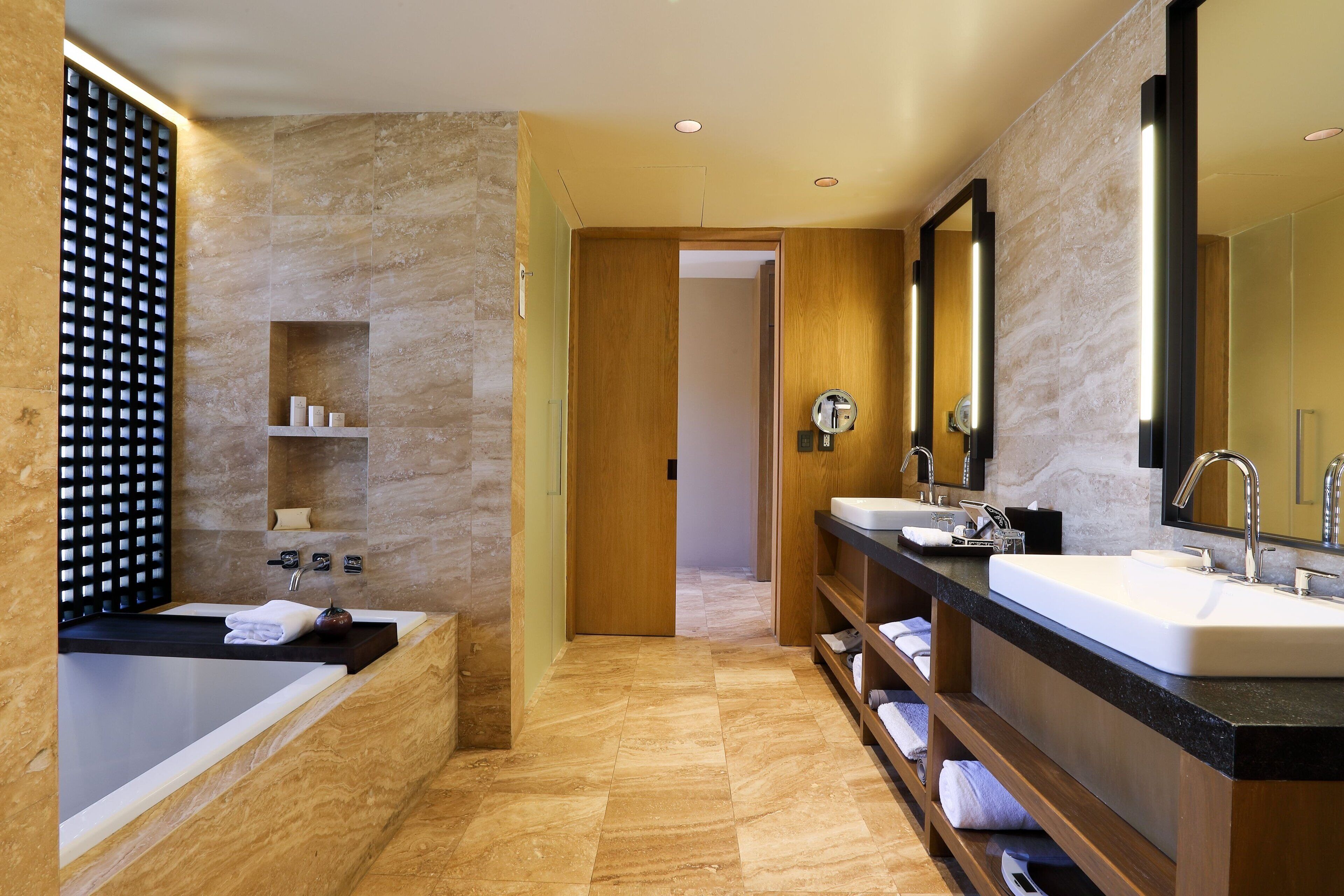 A modern bathroom with a bathtub, two sinks, and a large mirror.