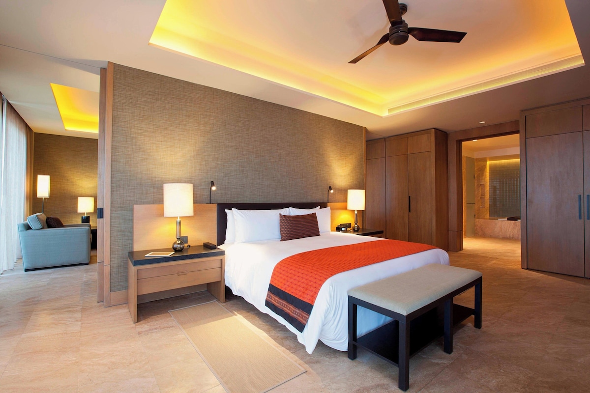 Une chambre d’hôtel moderne avec un grand lit, des tables de chevet avec des lampes, un ventilateur de plafond et une vue sur la salle de bain.