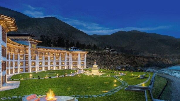 A large, multi-story hotel with a well-maintained courtyard, a central fire feature, and a mountain backdrop. - Le Meridien Paro, Riverfront (Paro)
