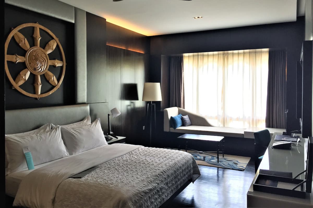 Habitació d'hotel moderna amb un llit gran, escriptori, cadira, ventilador de sostre i una finestra àmplia amb cortines.