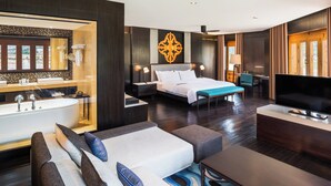 A modern hotel room with a large bed, a sitting area with a sofa and ottoman, a TV, a desk with a chair, and a bathroom with a bathtub and vanity. - Le Meridien Paro, Riverfront (Paro)