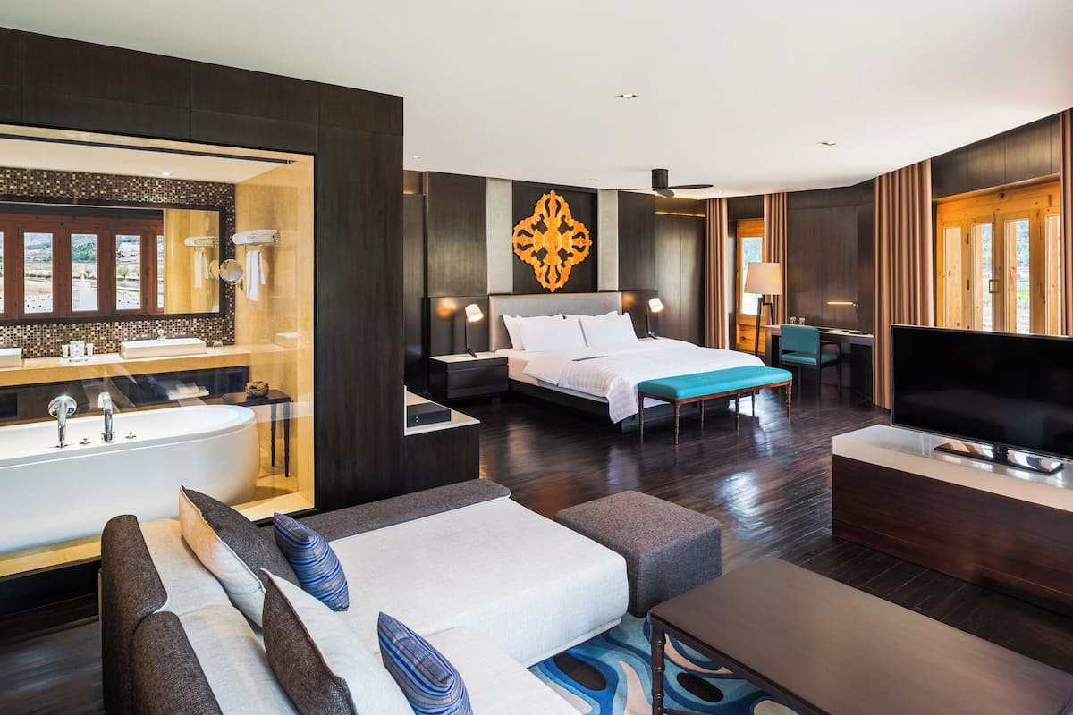 Habitació d'hotel moderna amb un llit gran, una zona de seients amb un sofà i un otomà, una televisió, un escriptori amb una cadira i un bany amb banyera i tocador.