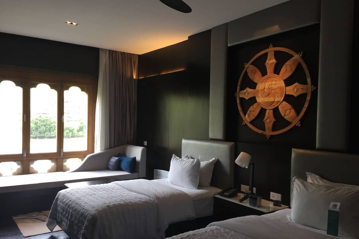 Habitació d'hotel amb dos llits, una finestra gran amb cortines, un timó de vaixell fixat a la paret i una taula de nit amb una làmpada i un telèfon.