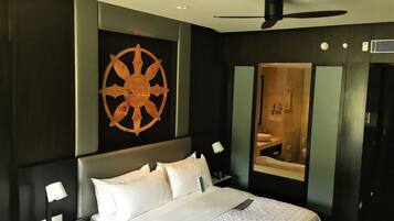 A hotel room with a bed, bedside tables, a wall-mounted ship's wheel, a ceiling fan, and a mirror.