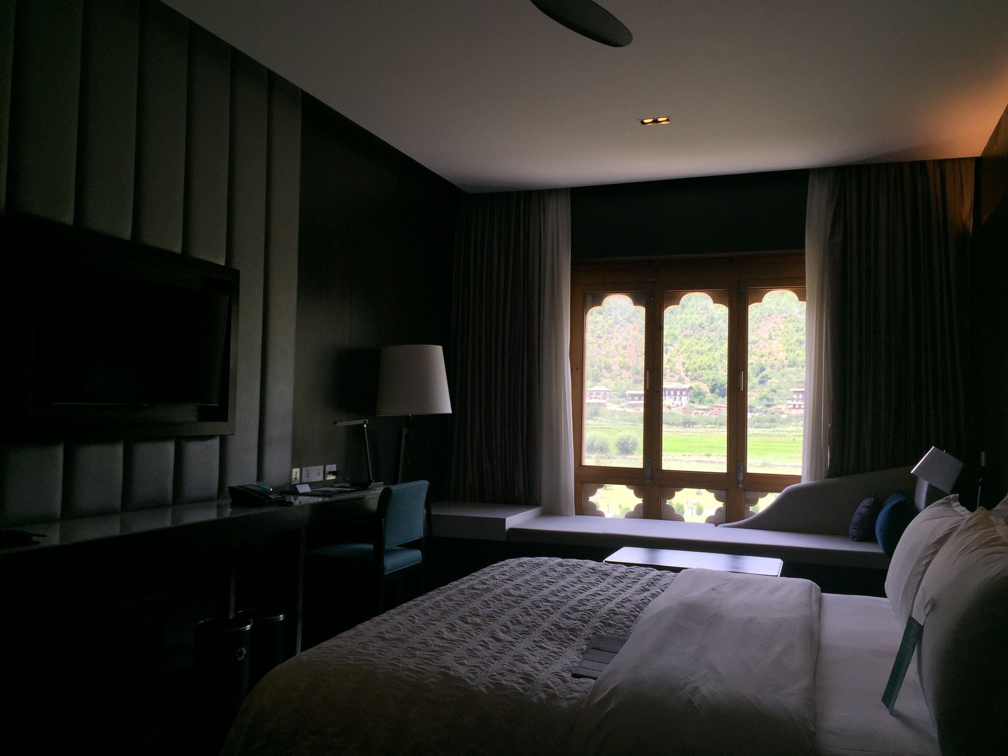 A hotel room with a bed, a desk, a chair, a television, and a window with curtains.