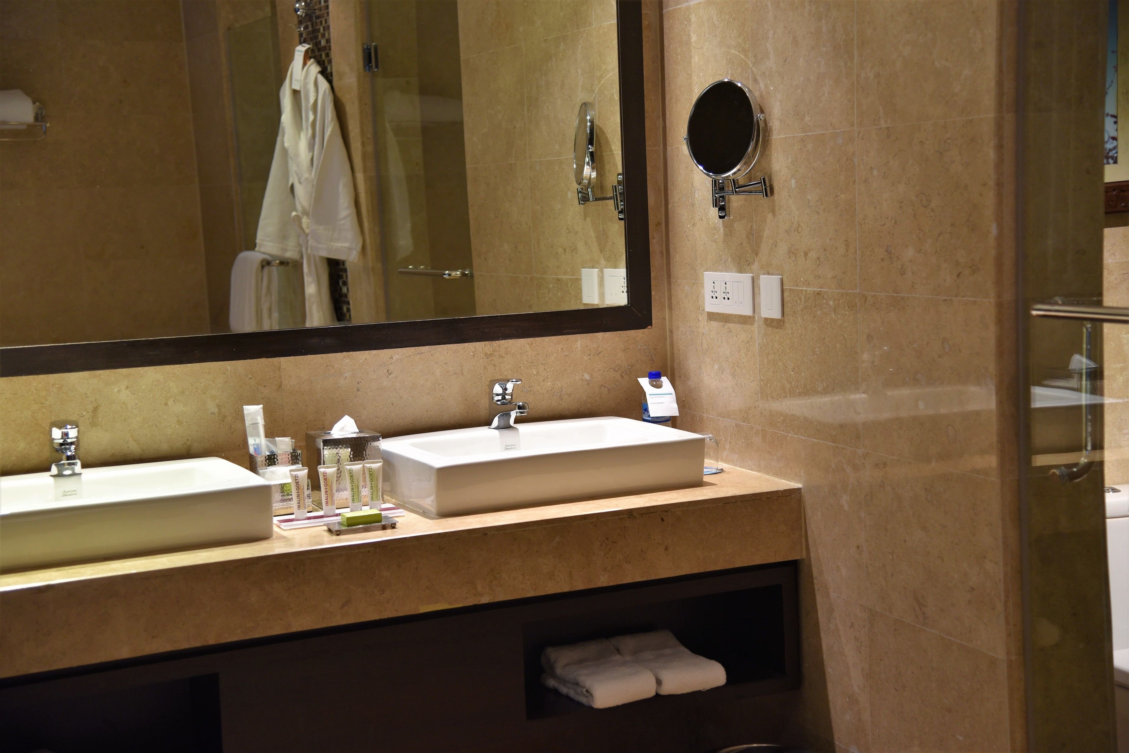 A bathroom with a large mirror, two sinks, a towel rack, and a glass shower enclosure.