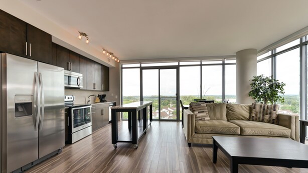 A modern kitchen with stainless steel appliances, a dining area with a sofa and table, and large windows offering a city view.