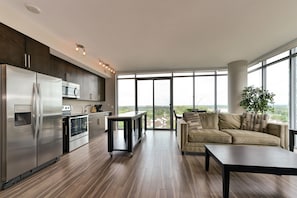 A modern kitchen with stainless steel appliances, a dining area with a sofa and table, and large windows offering a city view.