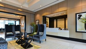 A modern lobby with a reception desk, patterned chairs, and a potted plant.