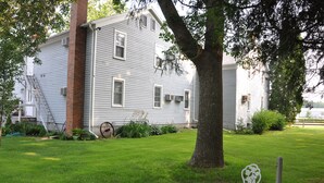 A two-story house with a brick chimney, a well-maintained lawn, and a small patio with white outdoor furniture. - Die Heimat Country Inn (Homestead)