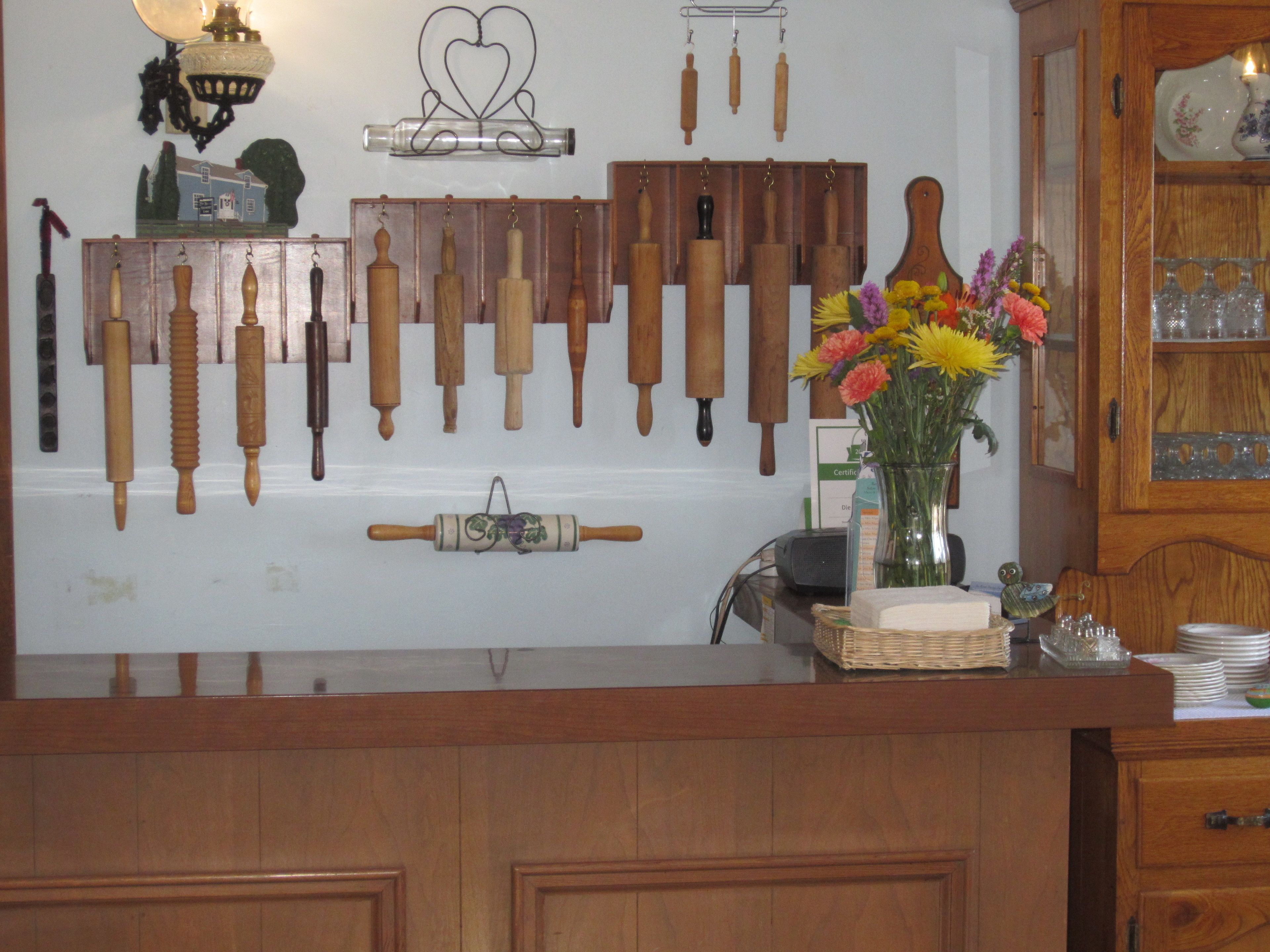 A kitchen with wooden cabinets, a rolling pin, various kitchen utensils, and a vase with flowers on the counter.
