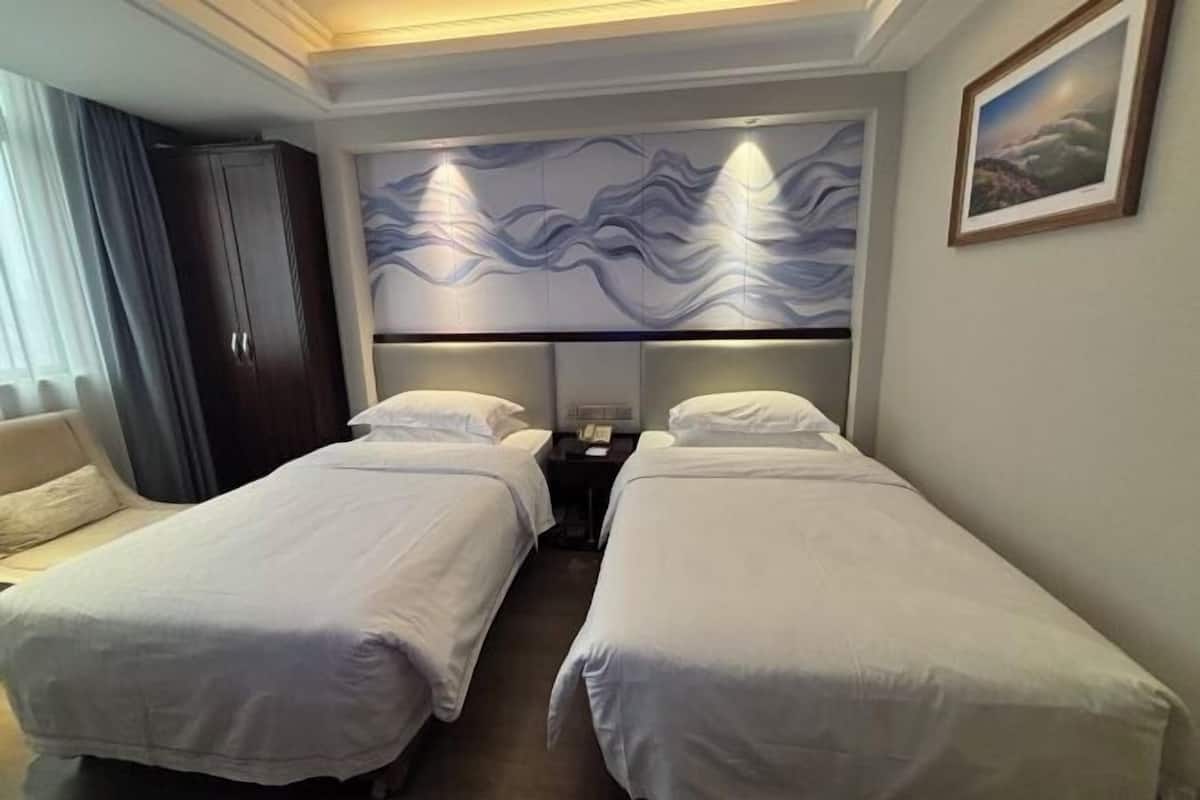 Ein Hotelzimmer mit zwei Einzelbetten, einem Schlafsofa, einem dunklen Kleiderschrank und einer Wand mit einem Wellenmuster.