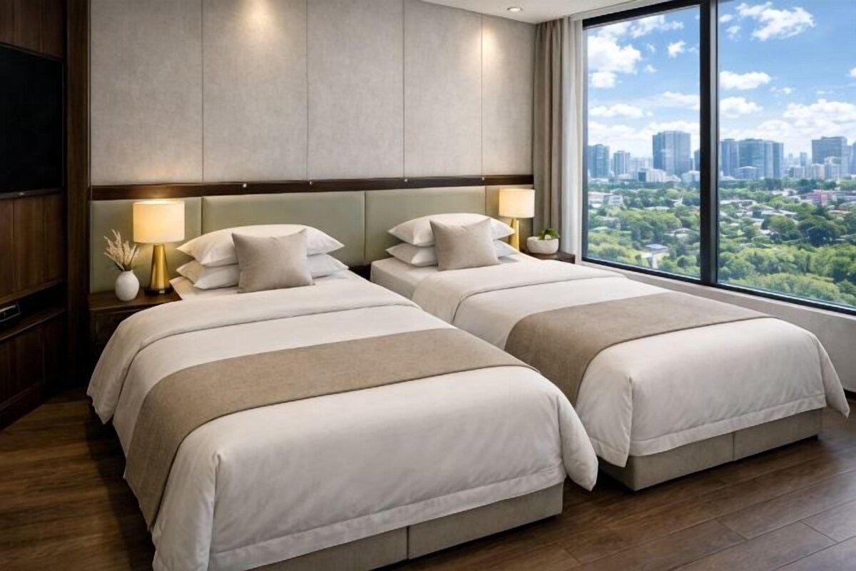 Habitación de hotel con dos camas, un ventanal grande con vista a la ciudad y un televisor a la izquierda.